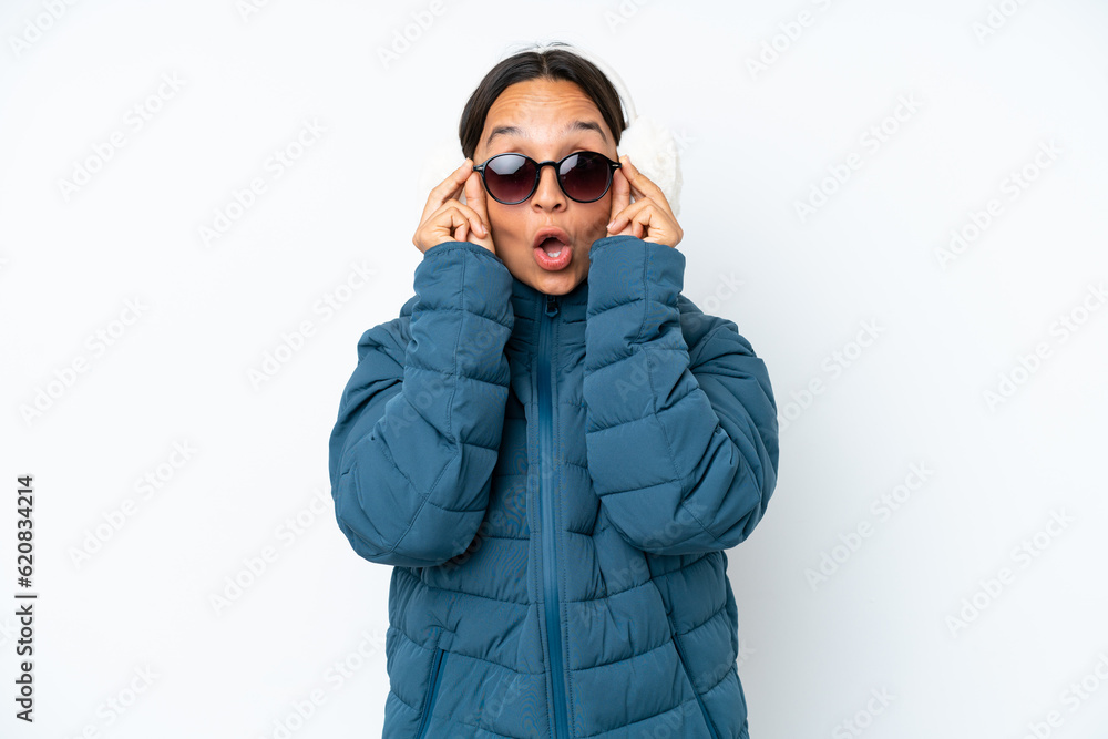 Young hispanic woman wearing a winter earmuffs isolated on white background with glasses and surprised Young hispanic woman wearing a winter earmuffs isolated on white background with glasses and surprised