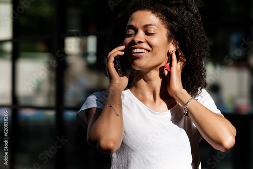 Smiling woman talking by phone in the street.