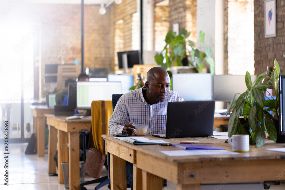 Happy african american casual businessman using laptop and having lunch in office Happy african american casual businessman using laptop and having lunch in office