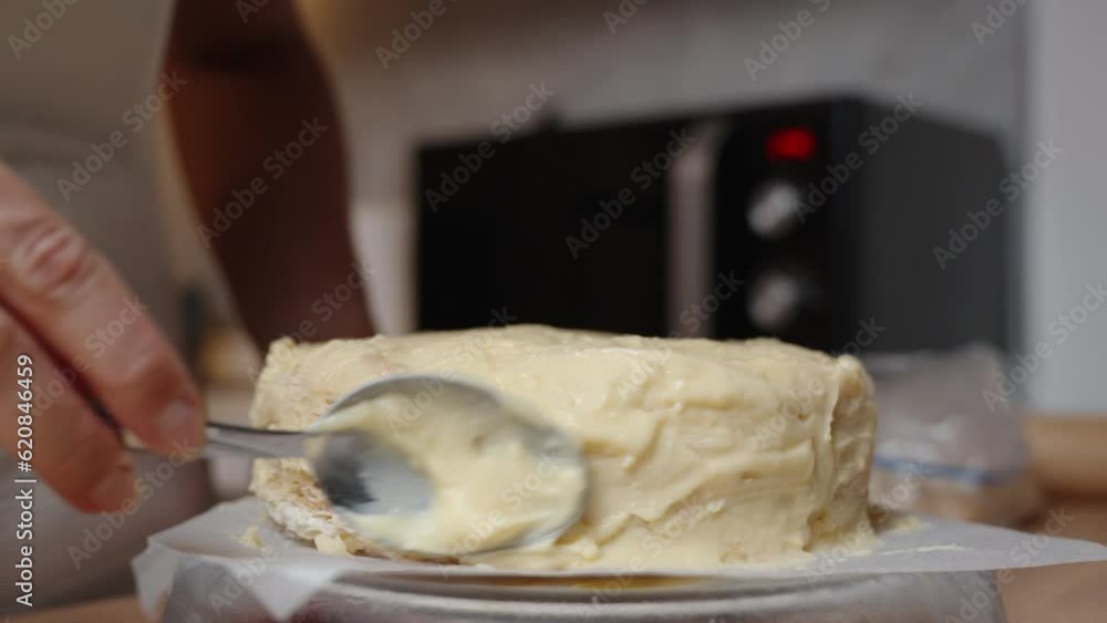 The woman spreads the cream in a circular motion on the Napoleon cake using a spoon. Close-up view. The woman spreads the cream in a circular motion on the Napoleon cake using a spoon. Close-up view.