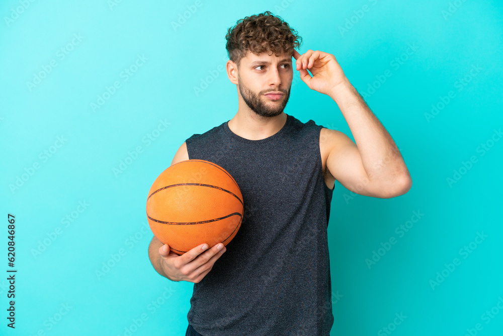 Handsome young man playing basketball isolated on blue background having doubts and thinking