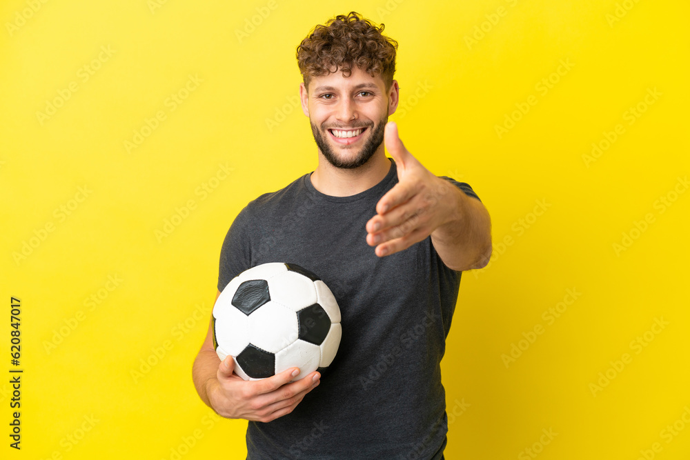 Handsome young football player man isolated on yellow background shaking hands for closing a good deal Handsome young football player man isolated on yellow background shaking hands for closing a good deal