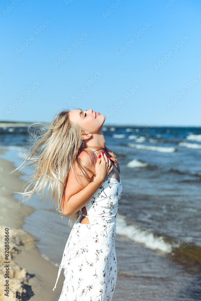 Happy blonde woman in free happiness bliss on ocean beach standing straight. Portrait of a female model in white summer dress enjoying nature during travel holidays vacation outdoors Happy blonde woman in free happiness bliss on ocean beach standing straight. Portrait of a female model in white summer dress enjoying nature during travel holidays vacation outdoors