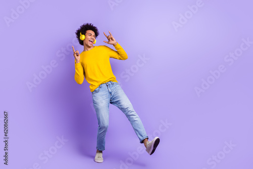 Full size photo of excited carefree person listen music headphones show heavy metal symbol empty space isolated on violet color background