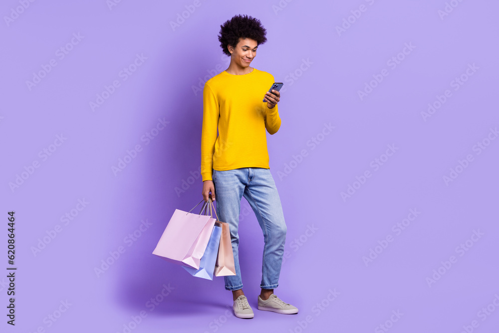 Fototapeta premium Full length body view cadre of young guy student shopping black friday read more propositions phone isolated on purple color background