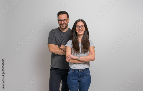 Portrait of smiling young couple wearing eyeglasses and casuals standing confidently against background. Joyful handsome man and beautiful woman posing with arms crossed