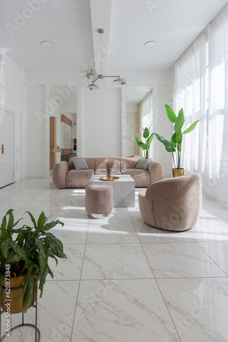 Fototapeta Naklejka Na Ścianę i Meble -  living room with soft beige furniture in a light luxury interior design of a modern apartment in a minimalist style with marble trim and huge windows. daylight inside.