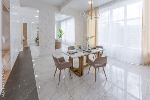 stylish kitchen and a set dining table in a light luxury interior design of a modern apartment in a minimalist style with marble trim and huge windows. daylight inside. © 4595886