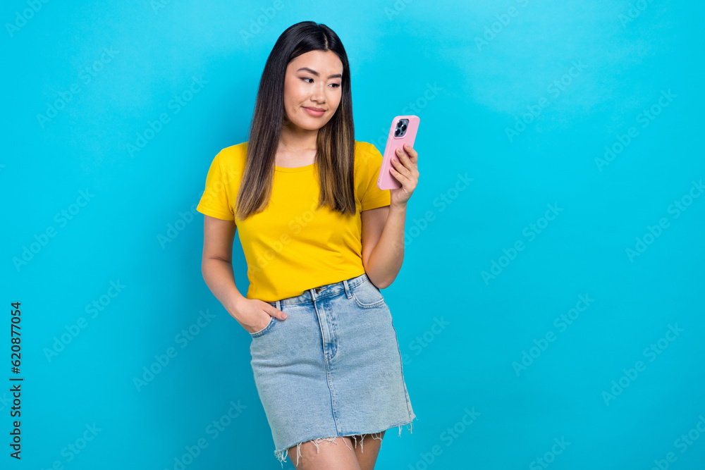Photo of satisfied girl dressed yellow t-shirt look at smartphone facebook twitter instagram whatsapp isolated on blue color background Photo of satisfied girl dressed yellow t-shirt look at smartphone facebook twitter instagram whatsapp isolated on blue color background