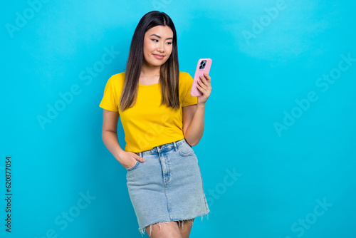 Photo of satisfied girl dressed yellow t-shirt look at smartphone facebook twitter instagram whatsapp isolated on blue color background