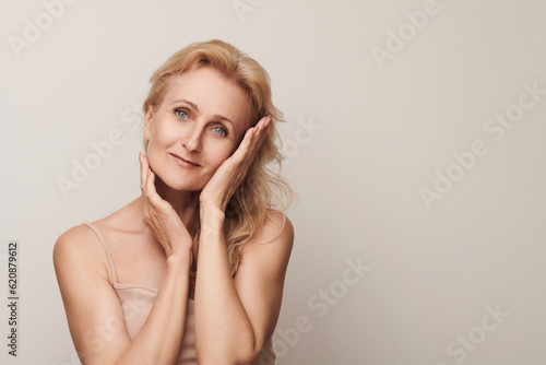 Beautiful blond middle aged woman smiling looking camera touching face portrait. Elegant mature lady no makeup 50 years old close-up isolated on white Women's health, cosmetology, skin care.