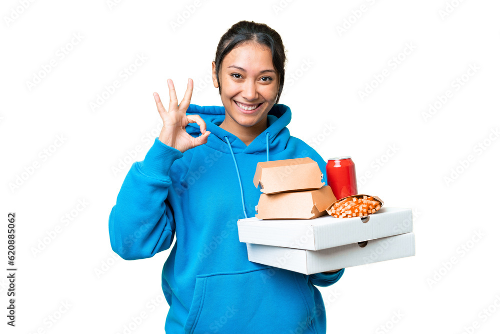 Young Uruguayan woman holding pizzas and burgers over isolated chroma key background showing ok sign with fingers Young Uruguayan woman holding pizzas and burgers over isolated chroma key background showing ok sign with fingers