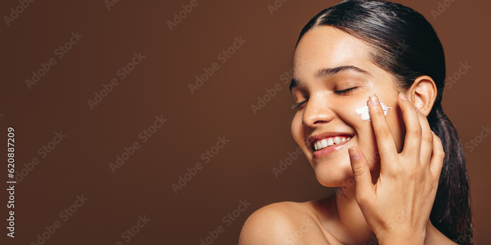 Moisturizing with face cream; young woman applies a beauty product on