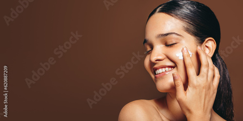 Fotografija Moisturizing with face cream; young woman applies a beauty product on her clear