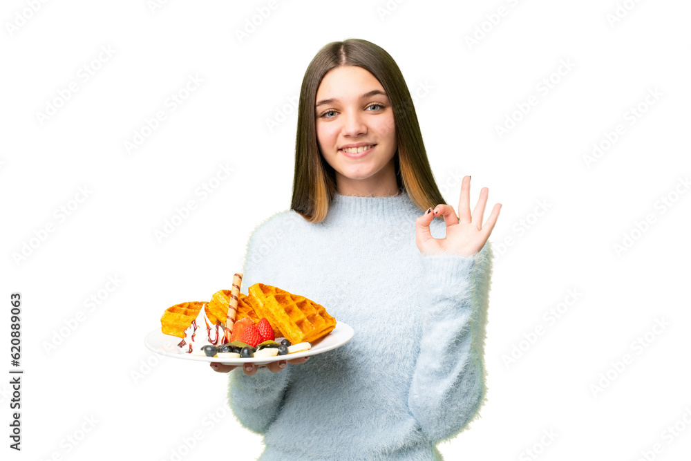 Teenager girl holding waffles over isolated chroma key background showing ok sign with fingers Teenager girl holding waffles over isolated chroma key background showing ok sign with fingers