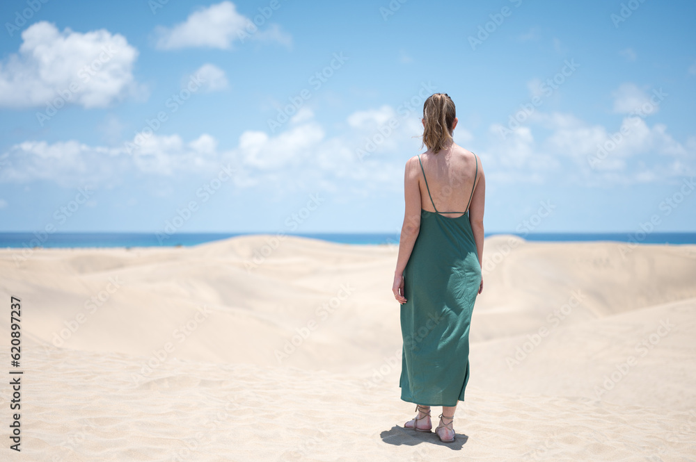 Blond young girl with green dress from behind on the beach dunes
