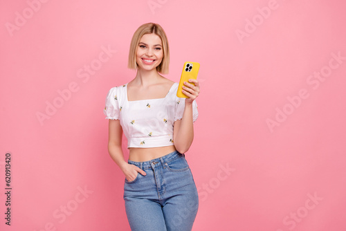 Photo of optimistic young girl wear jeans stylish top blouse writing email online shopping sms marketing isolated on pink color background
