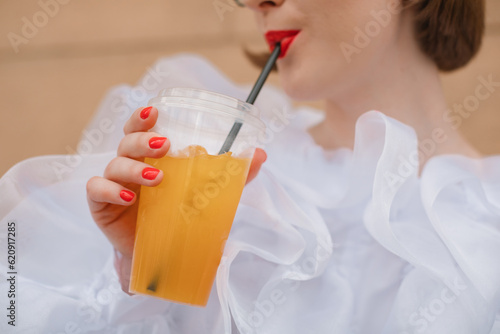Glamorous woman in a ruffled blouse standing outdoors drinking a fruit drink
