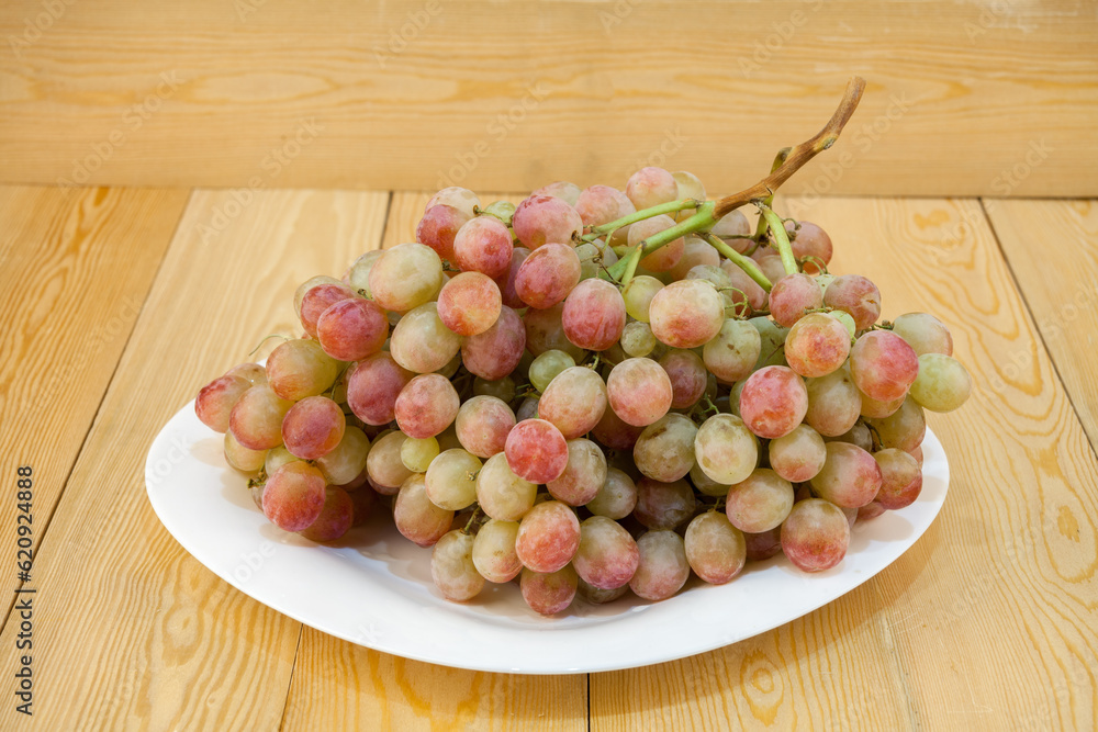 Grape. a bunch of grapes. Dark blue Isabella. and red grapes on a white saucer. on an isolated wooden background. Still-life. for the poster. Grape. a bunch of grapes. Dark blue Isabella. and red grapes on a white saucer. on an isolated wooden background. Still-life. for the poster.