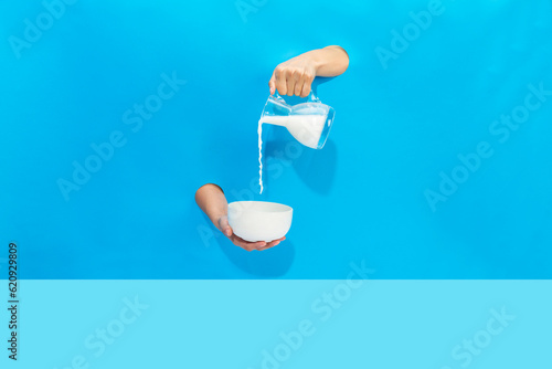 a hand pours milk from a jug into a bowl