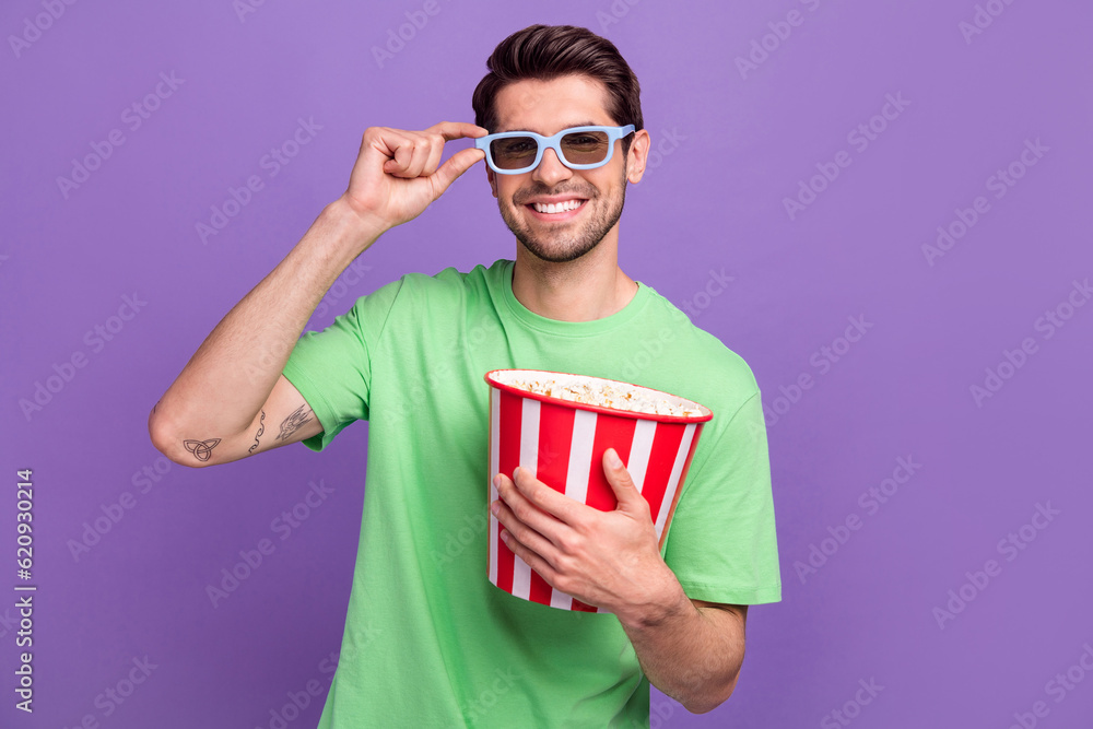 Photo of young guy stylish t-shirt hold bucket pop corn snack watching films in premiere cinema movies isolated on violet color background Photo of young guy stylish t-shirt hold bucket pop corn snack watching films in premiere cinema movies isolated on violet color background