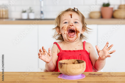 Excited toddler girl eating chocolate mousse with messy face