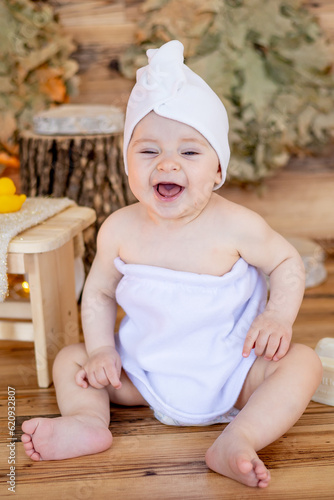 a cute little child in a towel and a turban on his head after bathing sits in a steam room in a bath with a washcloth and smiles or laughs