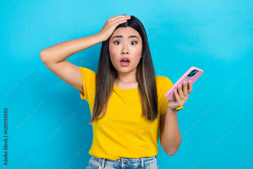 Naklejka premium Portrait of astonished woman dyed hairstyle wear stylish t-shirt arm on head staring hold smartphone isolated on blue color background