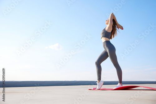 Sport and meditation. Young slim woman in comfortable sportswear training, doing stretching outdoors on warm sunny day
