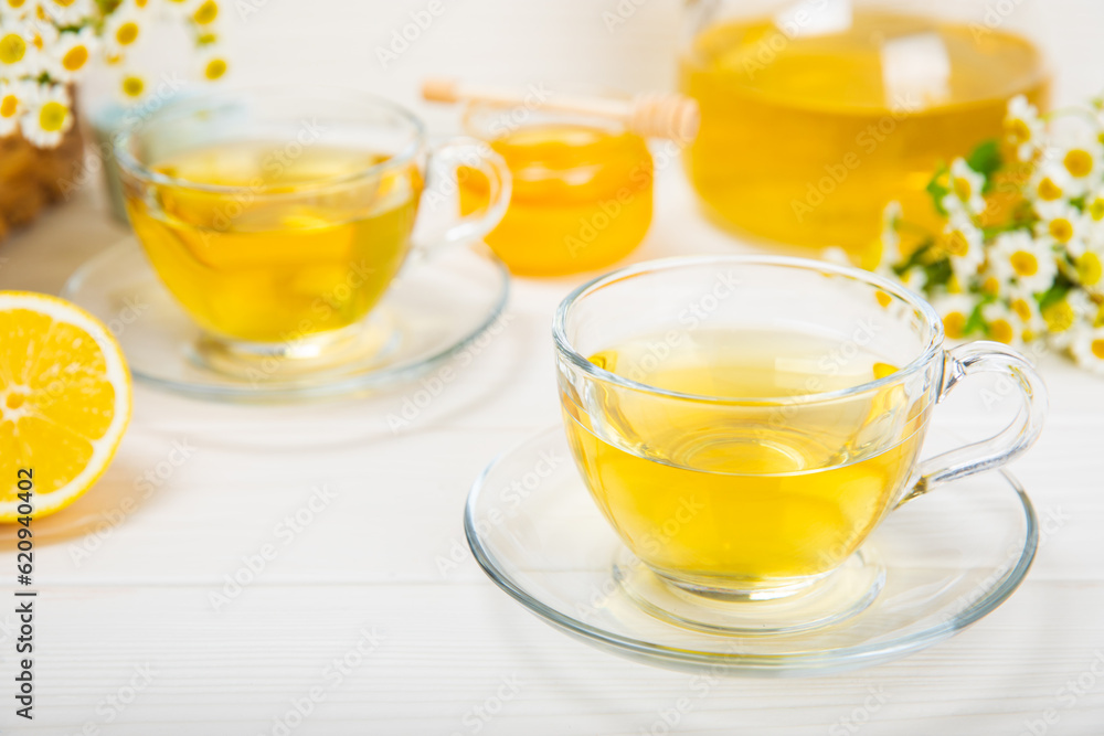 Chamomile herbal tea with flower buds, honey and lemon on a white wooden table and a bouquet of chamomile. Useful herbal, soothing drinks and natural healer concept. Immunity tea.Close up. Copy space. Chamomile herbal tea with flower buds, honey and lemon on a white wooden table and a bouquet of chamomile. Useful herbal, soothing drinks and natural healer concept. Immunity tea.Close up. Copy space.