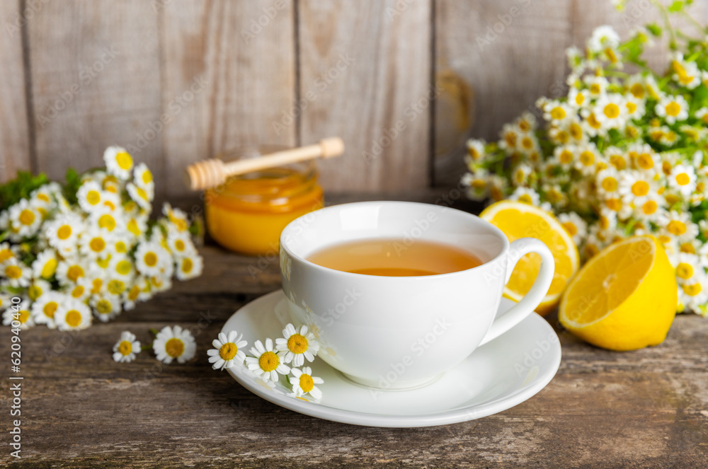 Chamomile herbal tea with flower buds, honey and lemon on a brown wooden table and a bouquet of chamomile. Useful herbal, soothing drinks and natural healer concept. Immunity tea.Close up. Copy space. Chamomile herbal tea with flower buds, honey and lemon on a brown wooden table and a bouquet of chamomile. Useful herbal, soothing drinks and natural healer concept. Immunity tea.Close up. Copy space.