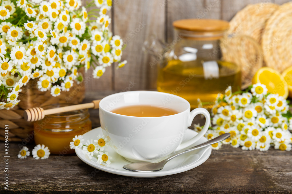 Chamomile herbal tea with flower buds, honey and lemon on a brown wooden table and a bouquet of chamomile. Useful herbal, soothing drinks and natural healer concept. Immunity tea.Close up. Copy space. Chamomile herbal tea with flower buds, honey and lemon on a brown wooden table and a bouquet of chamomile. Useful herbal, soothing drinks and natural healer concept. Immunity tea.Close up. Copy space.