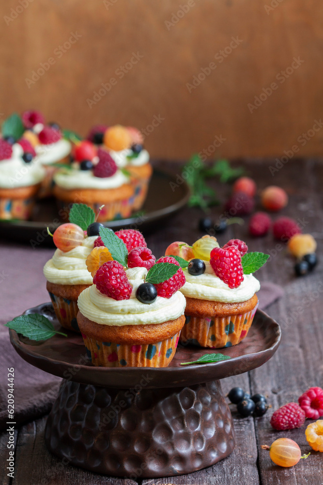 Cupcakes with butter cream and raspberry curd, decorated with berries on a wooden surface.
