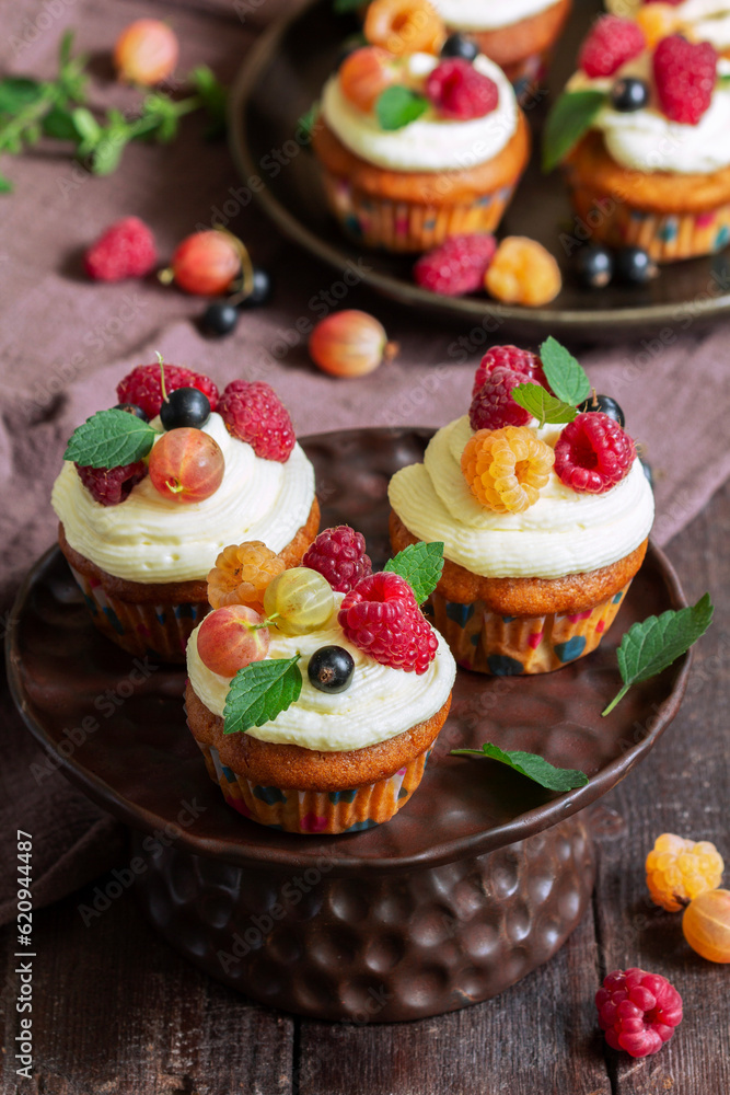 Cupcakes with butter cream and raspberry curd, decorated with berries on a wooden surface.
