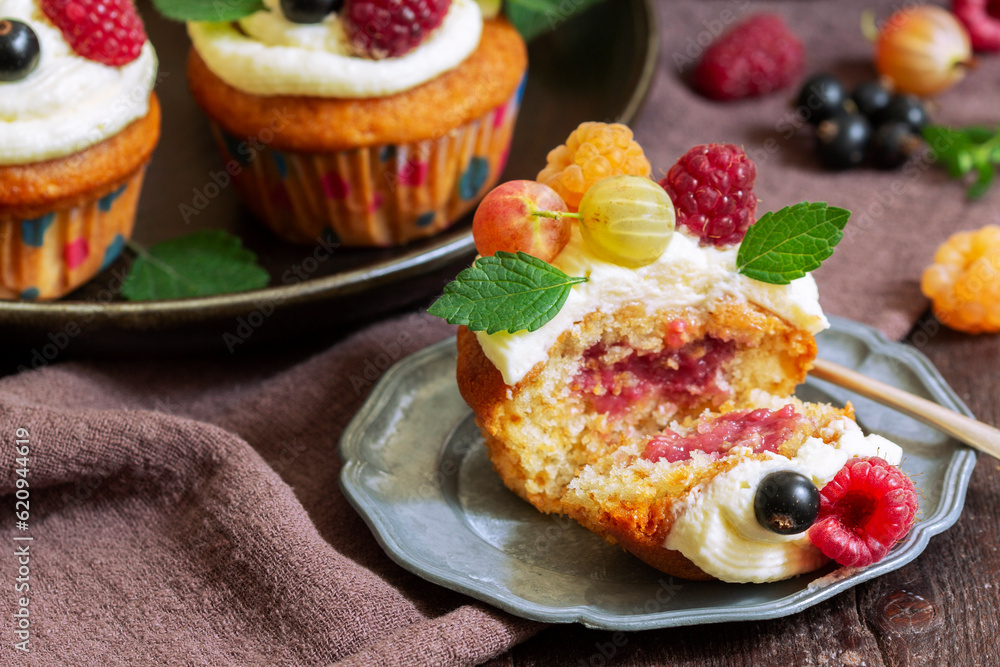 Cupcakes with butter cream and raspberry curd, decorated with berries on a wooden surface.