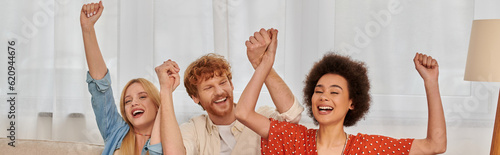 polyamorous relationship, cultural diversity, redhead man raising hands with multiracial female lovers, positivity, freedom and acceptance, love triangle, people in open relationship, banner photo