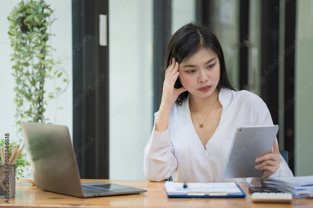 Attractive business Asian woman using a digital tablet while sitting at a workplace desk in an office. Attractive business Asian woman using a digital tablet while sitting at a workplace desk in an office.