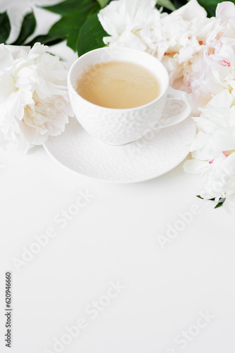 Morning coffee cup and white peonies flowers on white table with copyspace