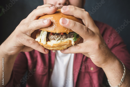 Unrecognizable man eating burger. No face closeup of male hands holds hamburger