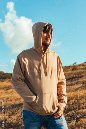 A young man portrait with a cream hoodie in dry grass and blue sky background from golden hour sunset, puerto rico © emaotx