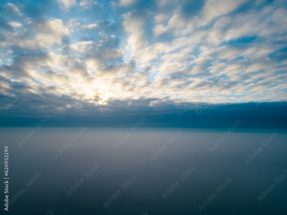 A striking aerial photo captures the stunning spectacle of the sun rising above a plush blanket of clouds. The ethereal image evokes an overwhelming sense of peace, vastness, and the grandeur of