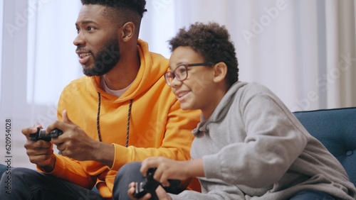 Cheerful African American brothers playing video games while sitting on couch at home