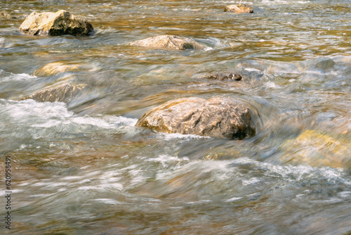 Rapid and powerful water flow between large rocks, close-up. Boulders in cold mountain river. Natural backgrounds