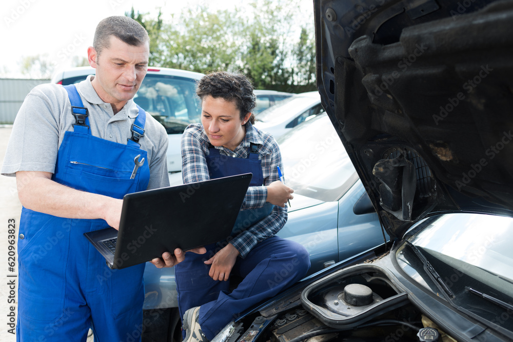 female and male mechanic using laptop for examining car engine female and male mechanic using laptop for examining car engine