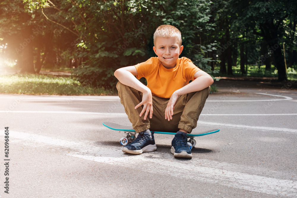 Outdoor activities for children.A cheerful young boy in bright clothes sits on a skateboard. Caucasian schoolboy on a walk. Front view Outdoor activities for children.A cheerful young boy in bright clothes sits on a skateboard. Caucasian schoolboy on a walk. Front view