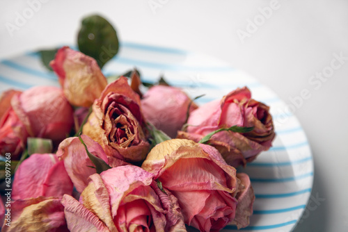 Several pink dried rose buds on a plate as interior decor. Group of beautiful dead flowers close-up as a concept of passed time, sadness, depression. Selective focus on the foreground