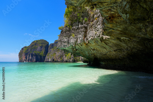 Small karstic cave in the cliffs surrounding the beach of Maya Bay, casting shade over the white sand and turquoise waters of the Andaman Sea on Koh Phi Phi Leh island, Krabi Province, Thailand