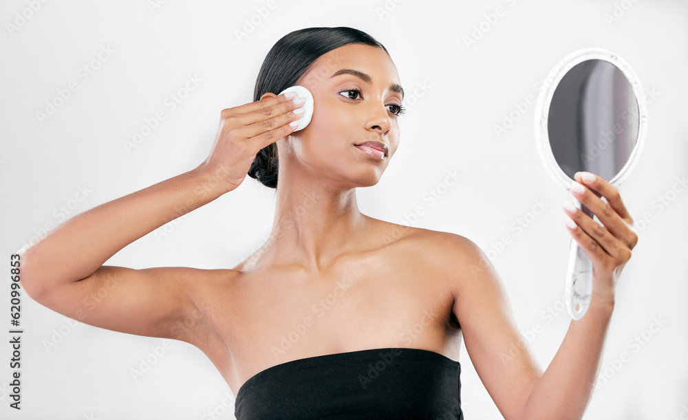 Woman, mirror and cotton pad for face, cosmetics and aesthetic skincare in studio on white background. Indian female model looking at reflection with beauty product for facial cleaning or dermatology Woman, mirror and cotton pad for face, cosmetics and aesthetic skincare in studio on white background. Indian female model looking at reflection with beauty product for facial cleaning or dermatology