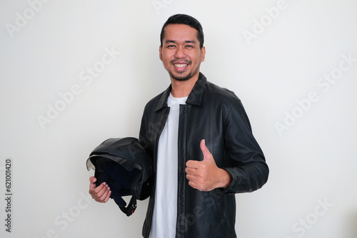 Adult Asian man smiling and give thumb up while holding motorcyle helmet photo