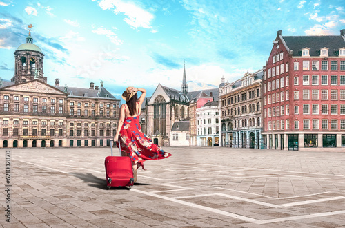 Photography Amsterdam Netherlands - Traveler woman in red dress and suitcase, walks on Dam square, Amsterdam on summer vacation in Holland - Europe summer travel concept